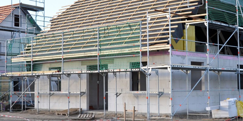 Haus im Rohbau mit Gerüst und Dachkonstruktion, Baustelle mit Baumaterialien
