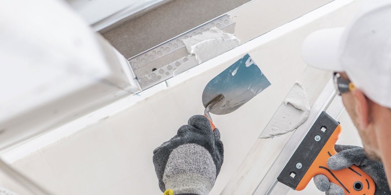 Handwerker beim Spachteln einer Rigipskante mit Glättkelle und Spachtelmasse