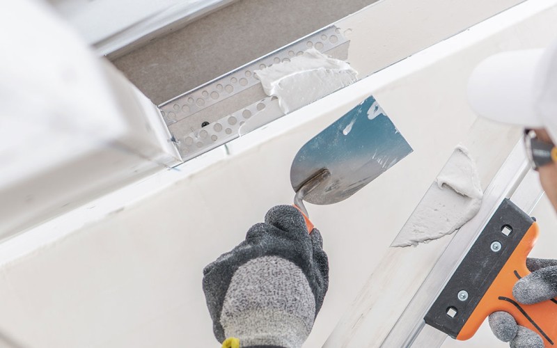 Handwerker beim Spachteln einer Rigipskante mit Glättkelle und Spachtelmasse