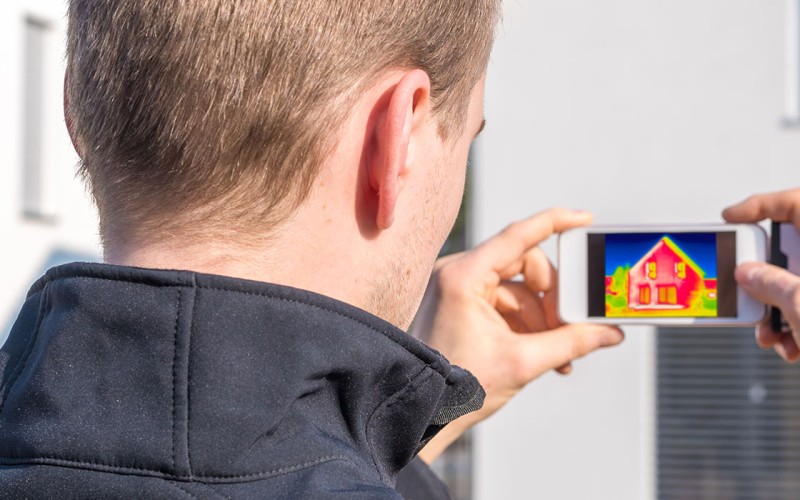 Mann hält Smartphone mit Wärmebildkamera auf ein Haus gerichtet